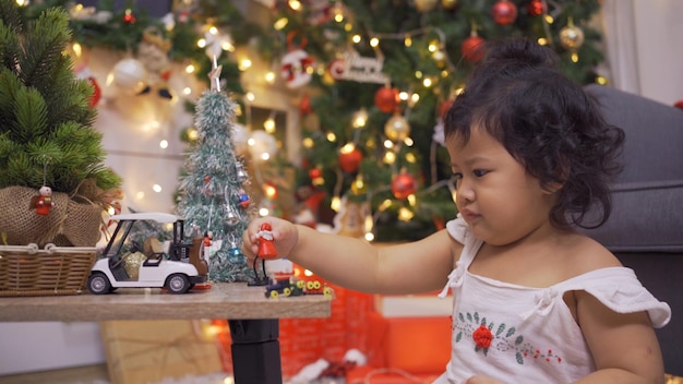 Gelukkig Aziatisch meisje veel plezier op eerste kerstdag. Kid met ouder met kerstboomversiering thuis op vakantie.