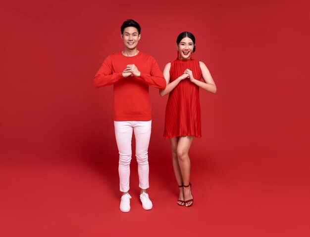 Gelukkig Aziatisch paar in rode vrijetijdskleding met gebaar van gelukwens die gelukkig nieuw jaar 2021 begroeten op heldere rode achtergrond.