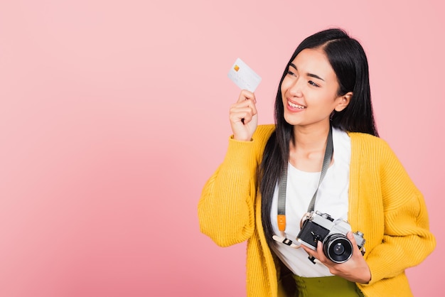 Gelukkig Aziatisch portret mooie jonge vrouw opgewonden lachende fotograaf met creditcard bank en retro vintage fotocamera klaar reizen geïsoleerd op roze achtergrond, toerisme en vakantie