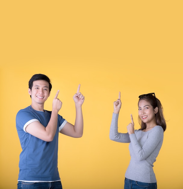 Gelukkig Aziatisch stel dat met de vingers omhoog wijst naar lege kopieerruimte voor tekst over gele achtergrond