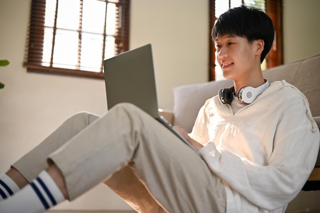 Gelukkig Aziatische man met behulp van laptop terwijl u ontspant in zijn woonkamer mensen een technologie