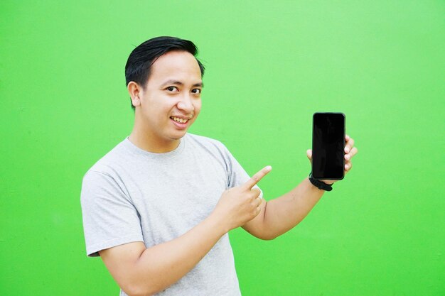 Foto gelukkig aziatische man permanent met armen over groene muur. knappe aziatische man met mobiel telefoonmodel