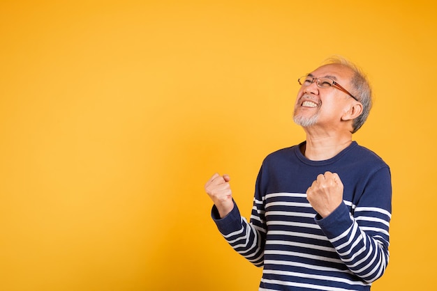 Gelukkig Aziatische oudere man met bril opgewonden zeg ja gebaar als winnaar