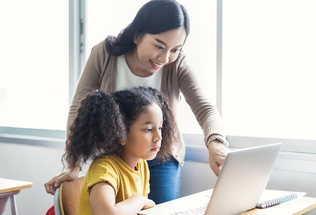 Gelukkig Aziatische vrouwelijke leraar helpt schoolkinderen met behulp van laptops in IT-klasse Onderwijs basisschool leren en technologie concept