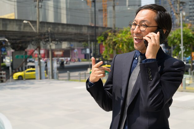 Gelukkig Aziatische zakenman praten aan de telefoon in de stad