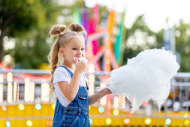 Gelukkig babymeisje dat suikerspin eet in het pretpark in de zomer