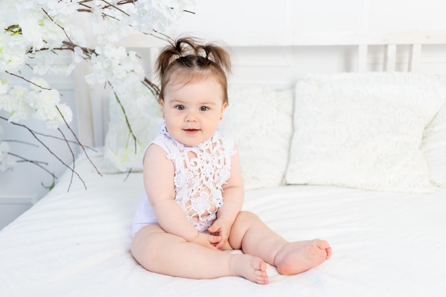 Gelukkig babymeisje in een witte bodysuit op het bed thuis in een lichte kamer glimlachend