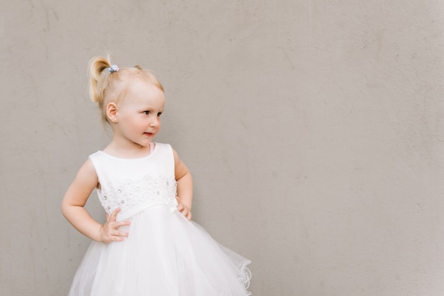 Gelukkig babymeisje in witte jurk op grijze muur