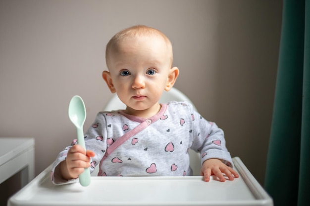 Gelukkig babymeisje met lepel zittend in kinderstoel thuis