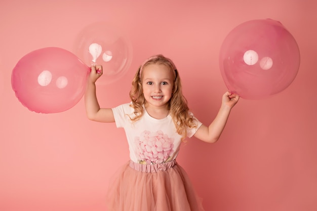 Gelukkig babymeisje op een roze achtergrond met ballonnen. viering. verjaardag