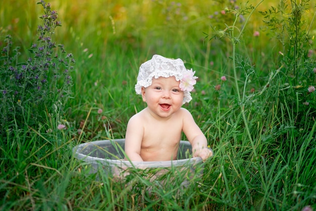 gelukkig babymeisje zes maanden oud baadt in een bak met schuim op een groen gazon in de zomer