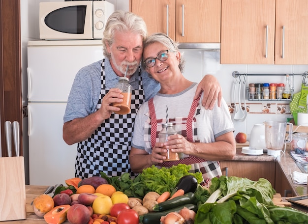 Gelukkig bejaard stel mensen die genieten van het sap dat zojuist is gemaakt. Man knuffelt de vrouw. Houten tafel met een grote groep kleurrijke groenten en fruit. Gezond eten