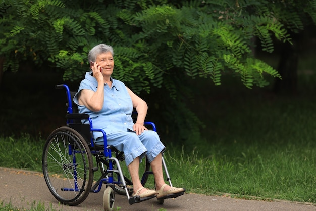 Gelukkig bejaarde gehandicapte vrouw zittend in een rolstoel buiten praten aan de telefoon