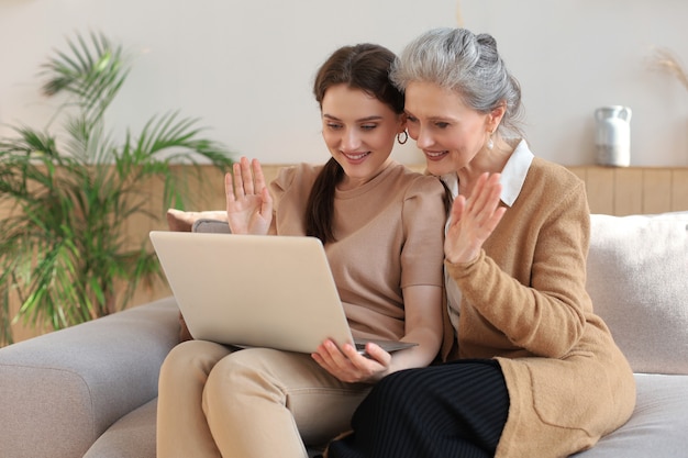 Gelukkig bejaarde middelste moeder zittend op de bank met haar dochter, laptop kijken. Jonge vrouw toont video, foto's aan mama, vertrouwde relaties. Familieconcept.