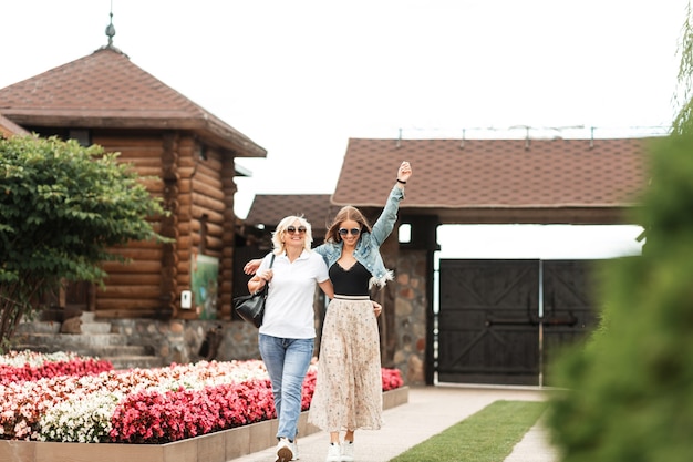 Gelukkig bejaarde moeder met vrolijke mooie dochter in modieuze casual jeans kleding wandelen samen in de natuur op het platteland. Familieweekend samen