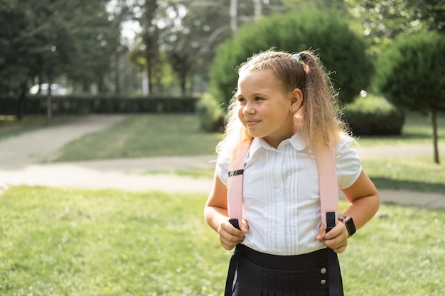 Gelukkig blond krullend schoolmeisje in schooluniform met roze rugzak terug naar school buiten.