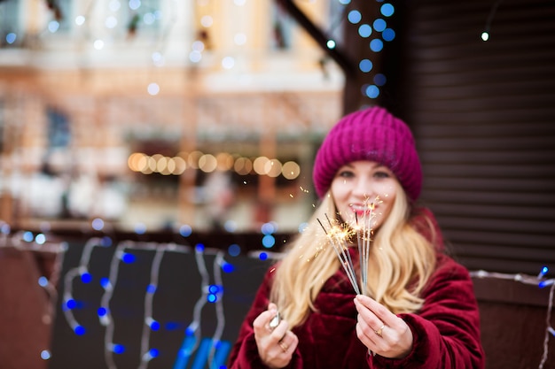 Gelukkig blond meisje met gloeiende bengaalse lichten op de kerstmarkt in kiev. vervagingseffect