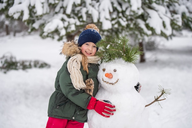 Gelukkig blond schattig kind meisje plaing met een sneeuwpop op een besneeuwde winterwandeling