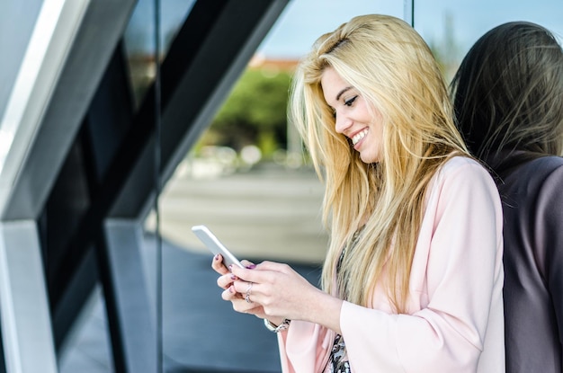 Gelukkig blonde jonge vrouw buiten met behulp van haar mobiele telefoon