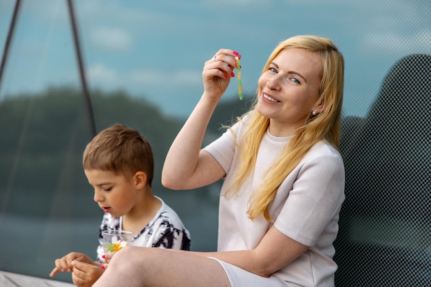 Gelukkig blonde vrouw en kleine jongen zittend op het terras en snoep eten Moeder en zoon genieten van tijd samen Positieve jonge moeder spelen tijd doorbrengen met haar schattige kind lachen met plezier Familie