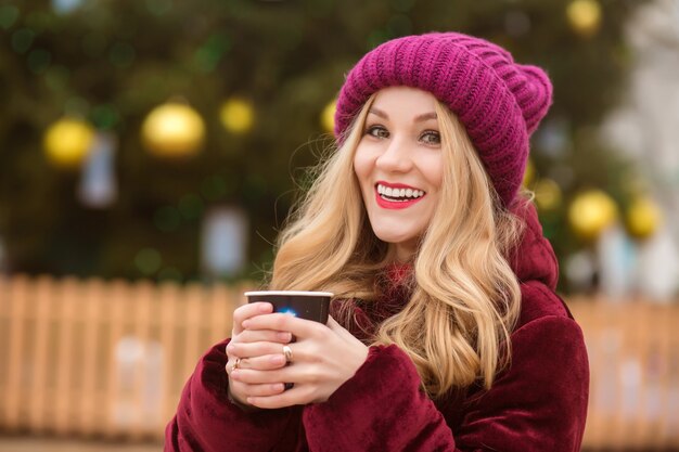 Gelukkig blonde vrouw gekleed in winterkleren en koffie drinken op straat