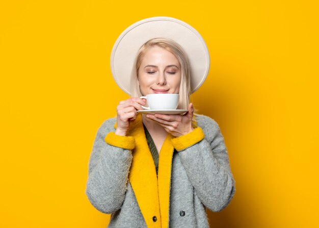 Gelukkig blonde vrouw in hoed en jas met kop koffie