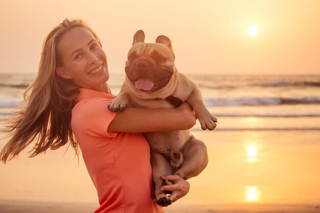 Gelukkig blonde vrouw met Franse bulldog op het strand van india goa bij zonsondergang