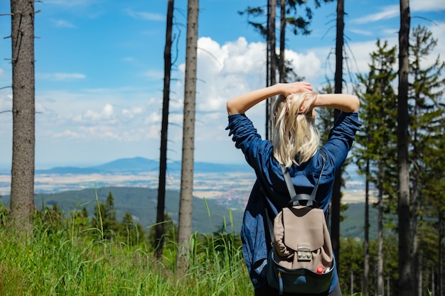 Gelukkig blondemeisje met packpack in bergen.