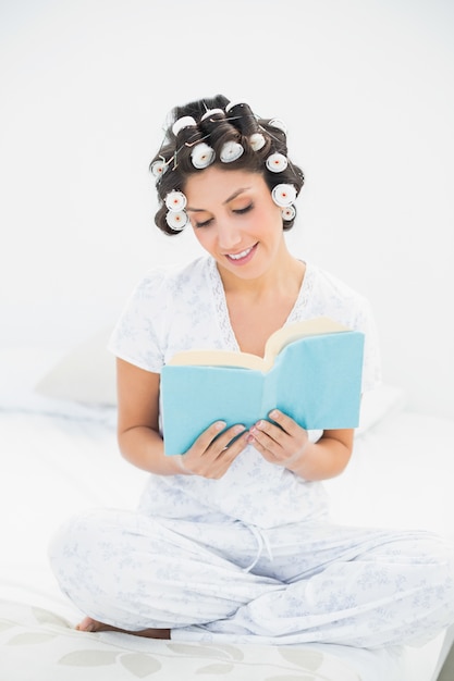 Gelukkig brunette in haarrollen die een boek op bed lezen