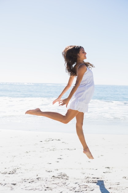 Gelukkig brunette in witte zonkleding die op het zand dansen