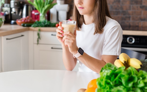 Gelukkig brunette vrouw zitten met zelfgemaakte glas smoothie en gezond fruit thuis keuken