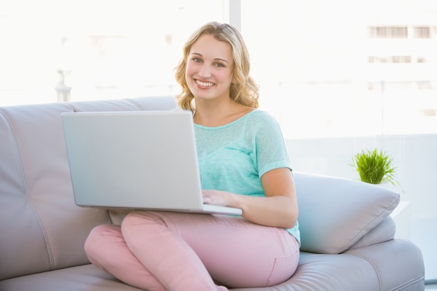 Gelukkig casual blonde ontspannen op de bank met behulp van de laptop