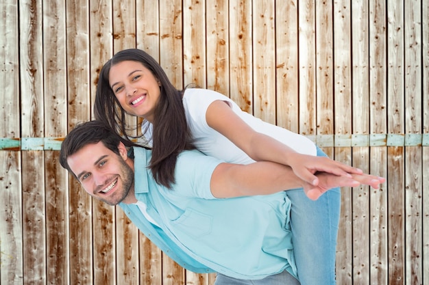 Gelukkig casual man die mooie vriendin piggy back geeft tegen houten achtergrond in bleek hout