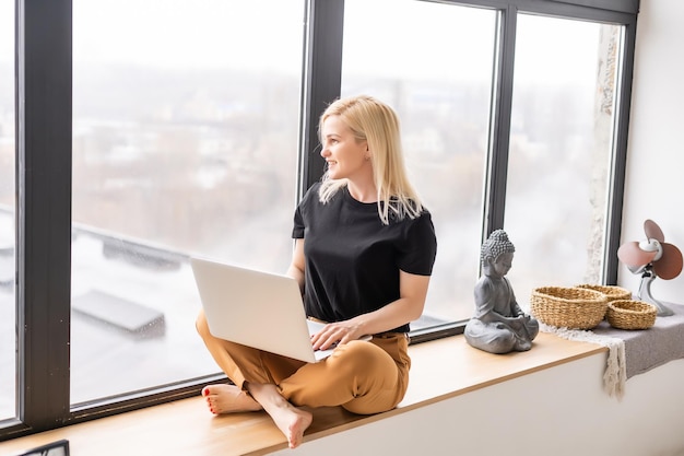 Gelukkig casual mooie vrouw die werkt op een laptop zittend in het huis.