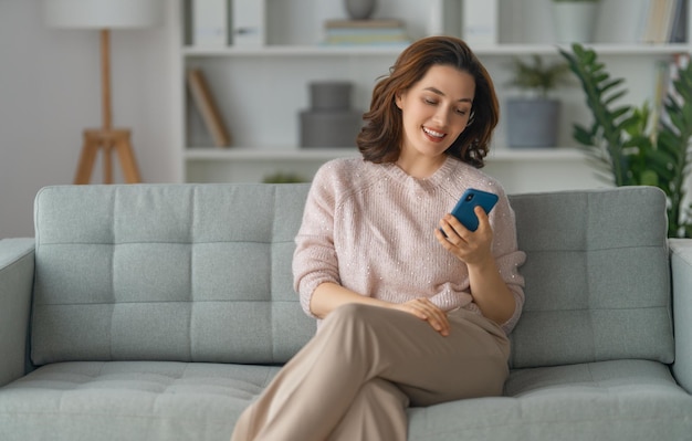 Gelukkig casual mooie vrouw gebruikt een telefoon zittend op een bank thuis