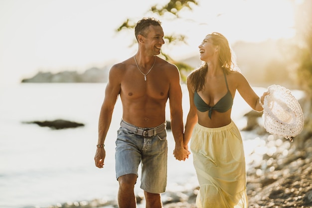 Gelukkig casual paar hand in hand, wandelen en zich speels voelen terwijl ze een zomerdag aan de kust doorbrengen.