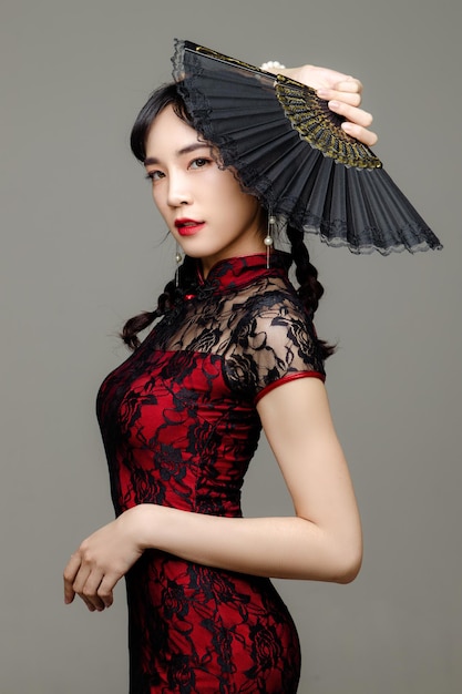 Gelukkig Chinees nieuwjaar Aziatische vrouw, gekleed in moderne cheongsam-jurk met een ventilator in de hand