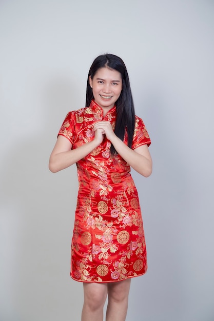 Gelukkig Chinees nieuwjaar. Mooie Aziatische vrouw, gekleed in traditionele cheongsam qipao jurk met gebaar van felicitatie geïsoleerd op lichtgrijs oppervlak met kopie ruimte