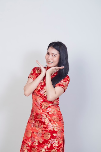 Gelukkig Chinees nieuwjaar. Mooie Aziatische vrouw, gekleed in traditionele cheongsam qipao jurk met gebaar van felicitatie geïsoleerd op lichtgrijs oppervlak met kopie ruimte