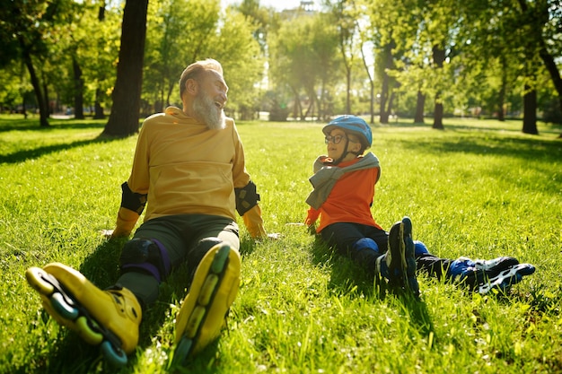 Gelukkig dolblij man en jongen rolschaatsers rusten op gras ingediend in het park