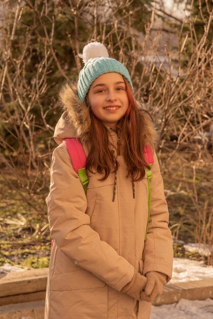 Gelukkig eenzaam aantrekkelijk jong meisje in warme kleding met rugzak staande in winter woud of park.
