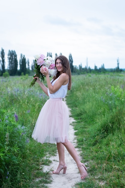Gelukkig elegante lachende vrouw houdt roze pioenrozen bloemen boeket in een veld