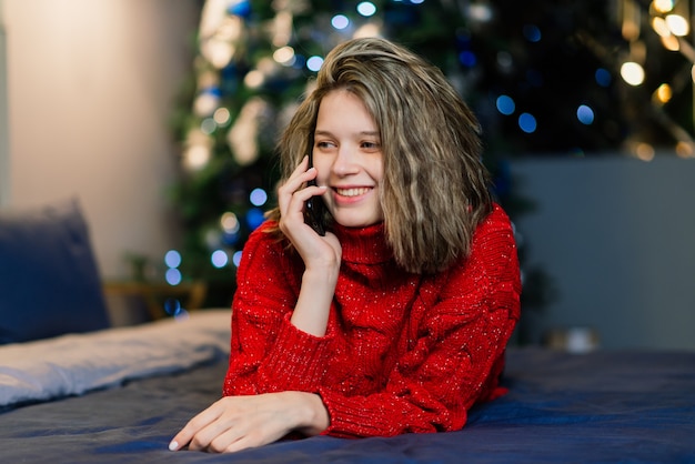 Gelukkig emotioneel verraste jonge vrouw door een kerstboom in een gezellige woonkamer, concept van geluk