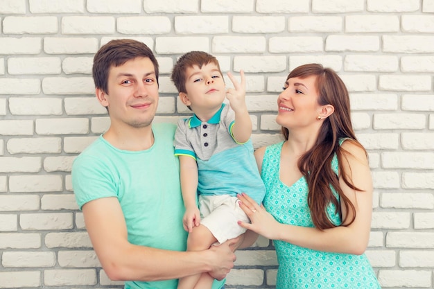 Gelukkig en glimlachend jong gezin portret op bakstenen muur achtergrond vader en moeder met kleine babyjongen ouders met kind