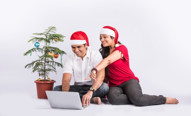 Gelukkig en jong Indiaas koppel op de bank met behulp van laptop tijdens het vieren van Kerstmis