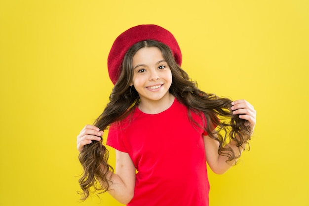 Gelukkig en mooi kid blij schattig gezicht schattig krullend haar gele achtergrond schoonheidstips voor netjes haar glimlachend kind kid meisje lang gezond glanzend haar draag rode hoed klein meisje met lang haar