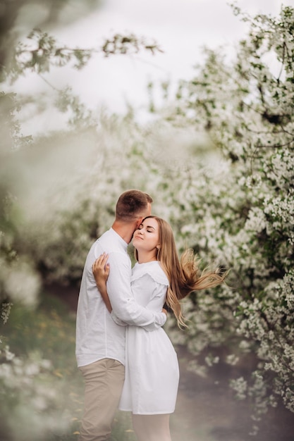 Gelukkig familie paar verliefd in een lente bloeiende appelboomgaard. Gelukkige familie geniet van elkaar tijdens het wandelen in de tuin. De man houdt de hand van de vrouw vast. Familie relaties