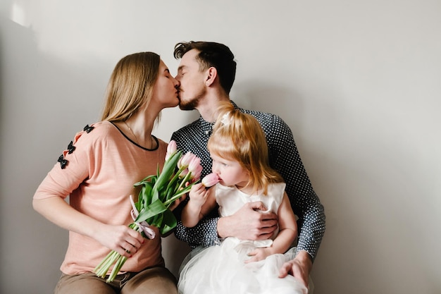 Gelukkig familieportret concept liefde voor een familievakantie moeder met bloemen vader knuffels dochter zittend in huis op een lichte achtergrond Emoties van geluk vrouw dag Moederdag