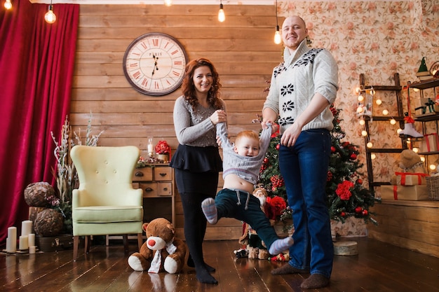 Gelukkig familieportret op Kerstmis, moeder, vader en zoon die thuis op de kinderstoel zitten, kerstversiering en cadeautjes om hen heen