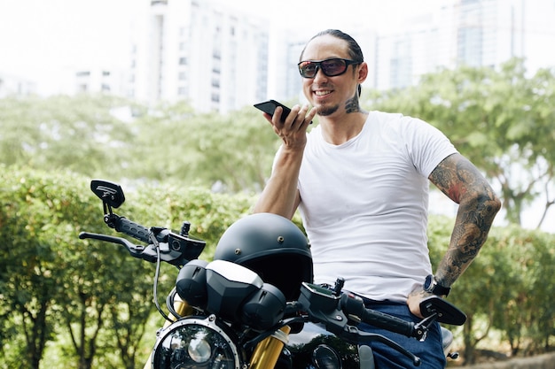 Gelukkig fit man zittend op een motorfiets en het opnemen van een spraakbericht voor een vriend